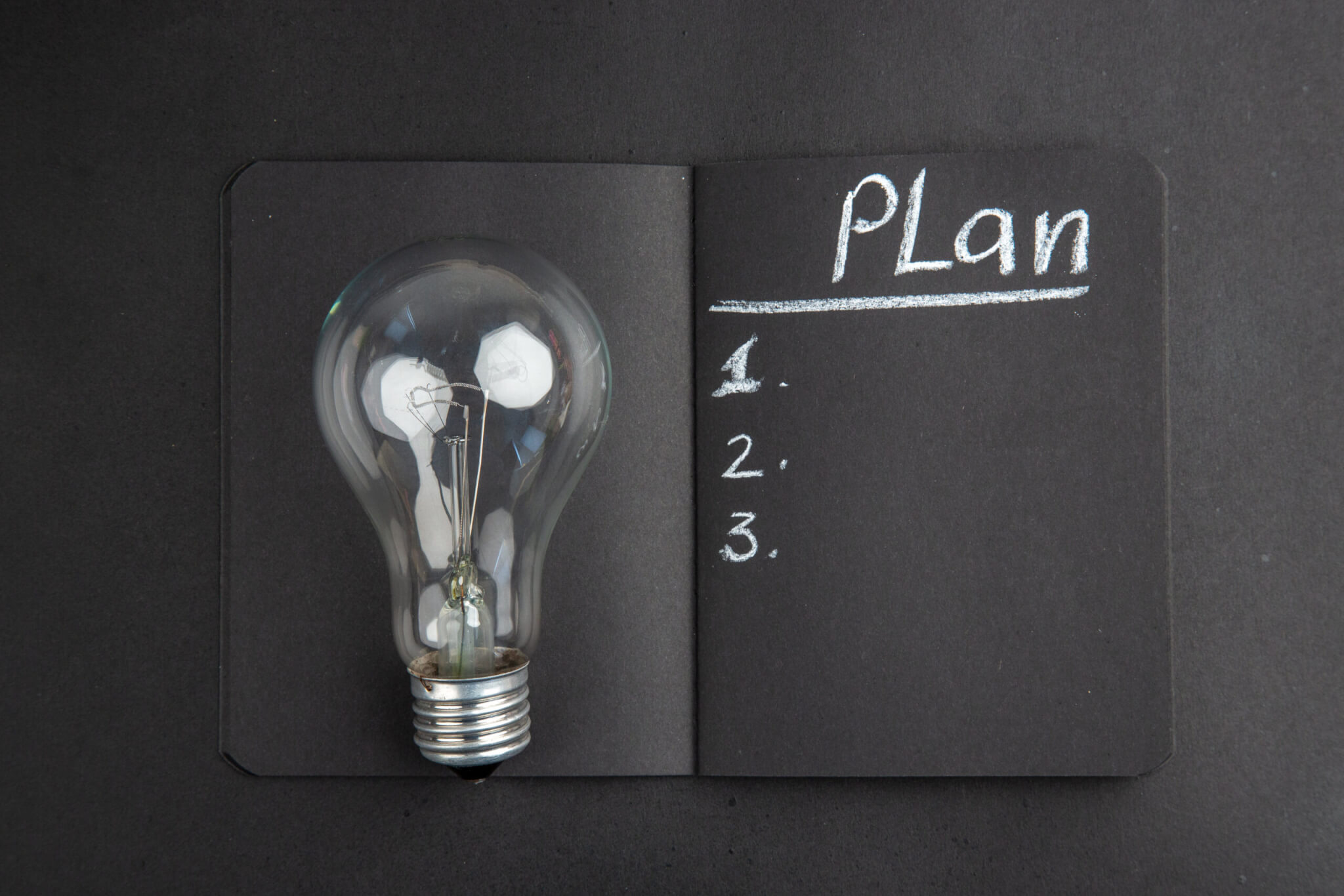top-view-plan-written-black-notepad-light-bulb-black-background